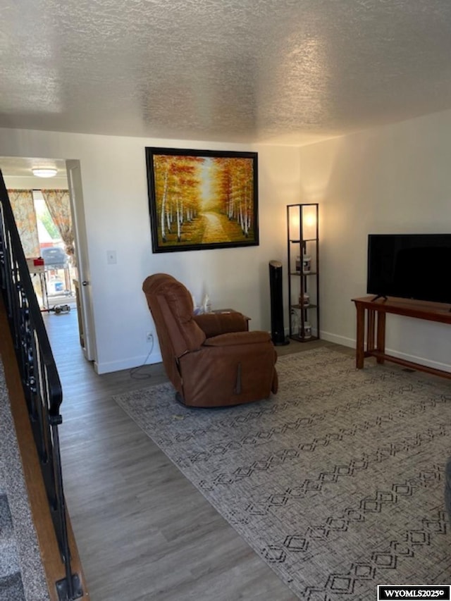 living area with a textured ceiling, baseboards, and wood finished floors