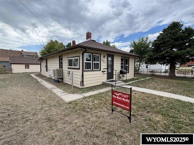 bungalow-style house featuring a front yard, central AC, fence, and a chimney