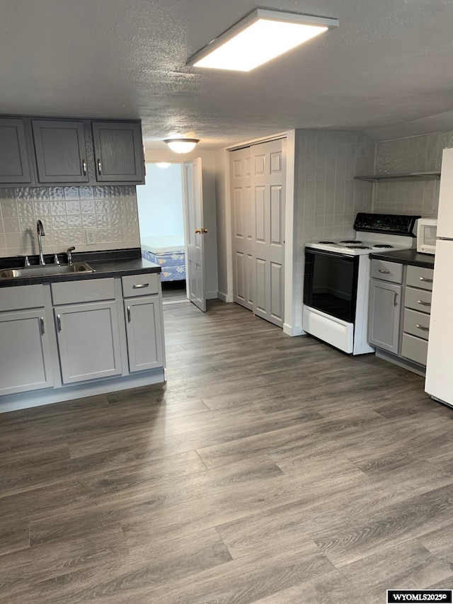 kitchen featuring dark wood-style floors, white appliances, dark countertops, and backsplash