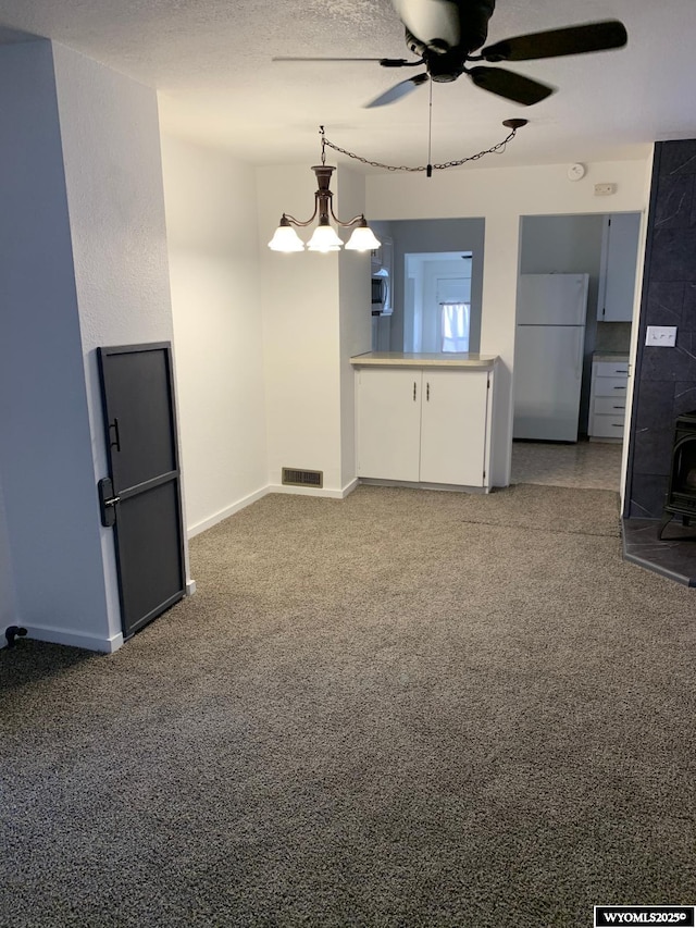 interior space featuring visible vents, a wood stove, a textured ceiling, baseboards, and ceiling fan with notable chandelier