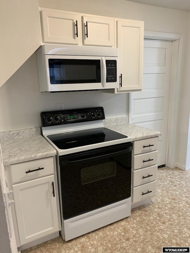 kitchen featuring white cabinets, white microwave, light stone countertops, black electric range, and light floors