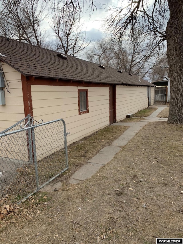 view of side of home with a shingled roof and fence