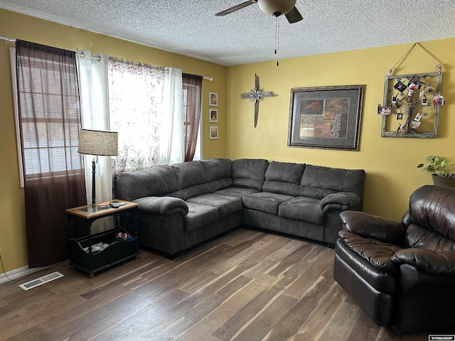 living area featuring ceiling fan, a textured ceiling, visible vents, and dark wood-type flooring