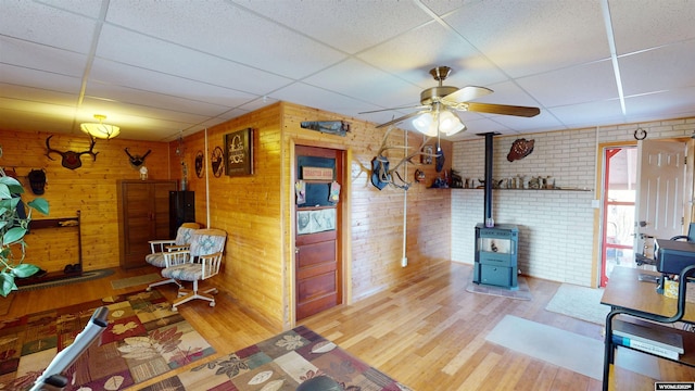 interior space with a wood stove, a drop ceiling, brick wall, and wood finished floors