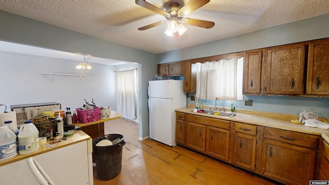 kitchen with pendant lighting, brown cabinets, light countertops, freestanding refrigerator, and a sink