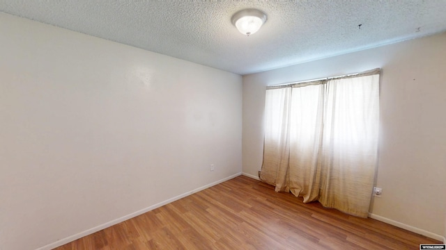 unfurnished room featuring a textured ceiling, baseboards, and wood finished floors