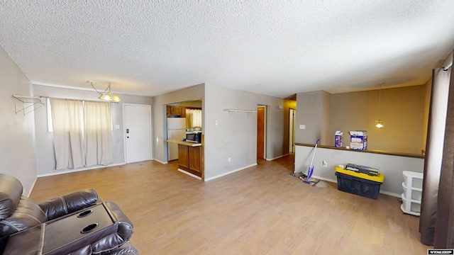 living area featuring a textured ceiling, light wood-type flooring, and baseboards