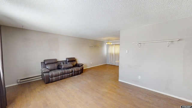 sitting room with a textured ceiling, a baseboard radiator, wood finished floors, and baseboards