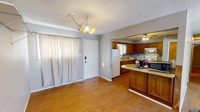 kitchen with light wood-style flooring, light countertops, freestanding refrigerator, brown cabinets, and stainless steel microwave