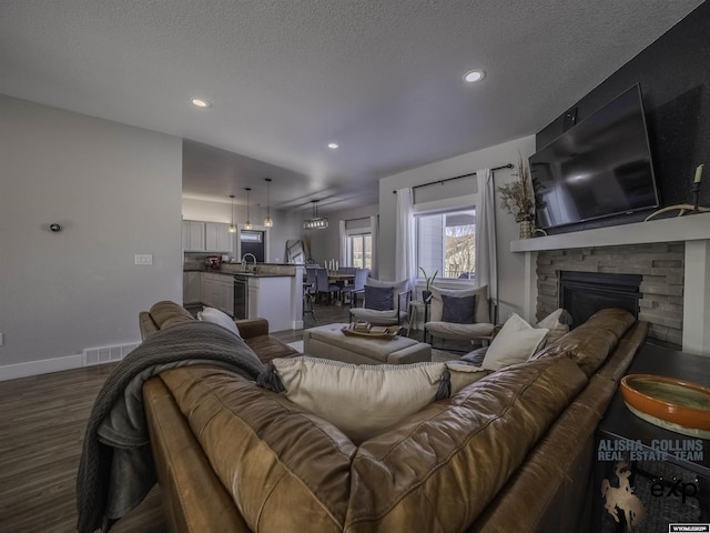 living room featuring a textured ceiling, a stone fireplace, dark wood-style flooring, visible vents, and baseboards