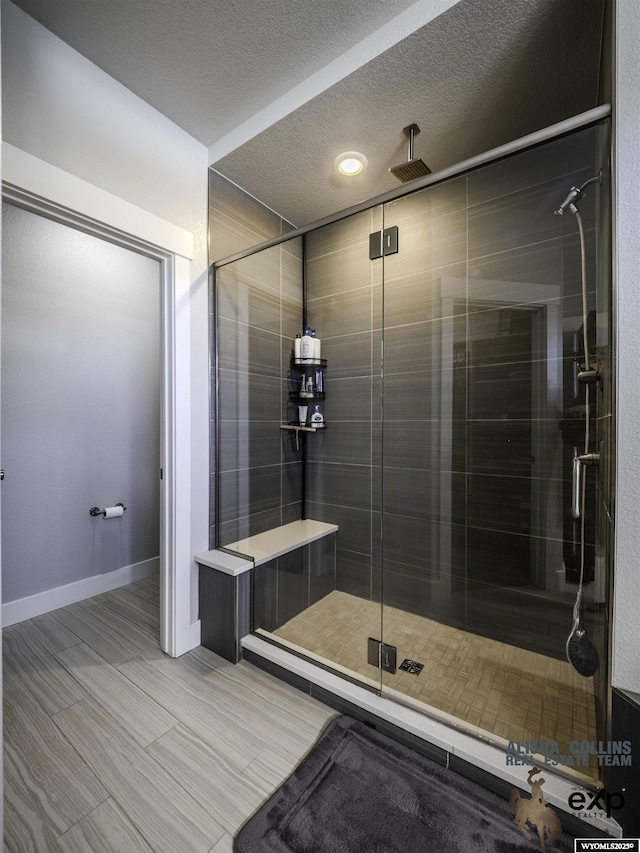 full bath featuring a textured ceiling, a shower stall, and baseboards