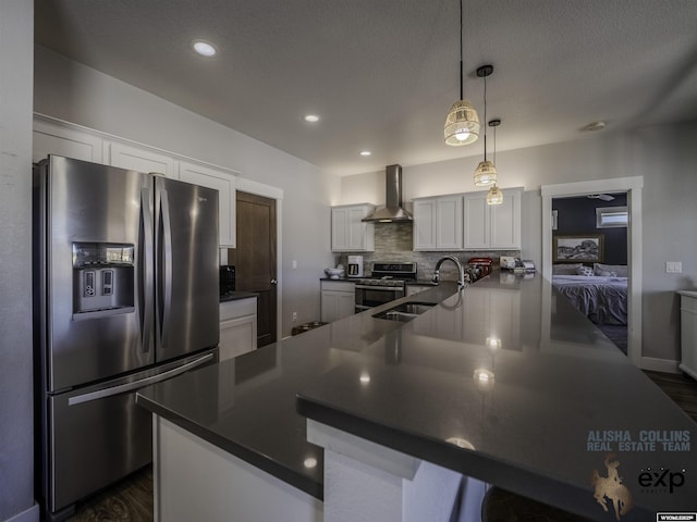 kitchen with a sink, white cabinetry, appliances with stainless steel finishes, wall chimney range hood, and dark countertops