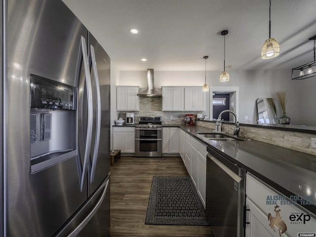 kitchen featuring dark countertops, appliances with stainless steel finishes, white cabinetry, a sink, and wall chimney range hood