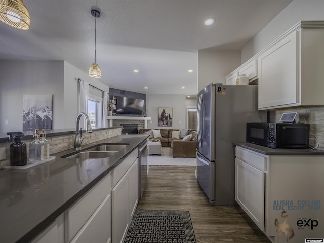 kitchen with stainless steel appliances, dark countertops, a sink, and white cabinetry