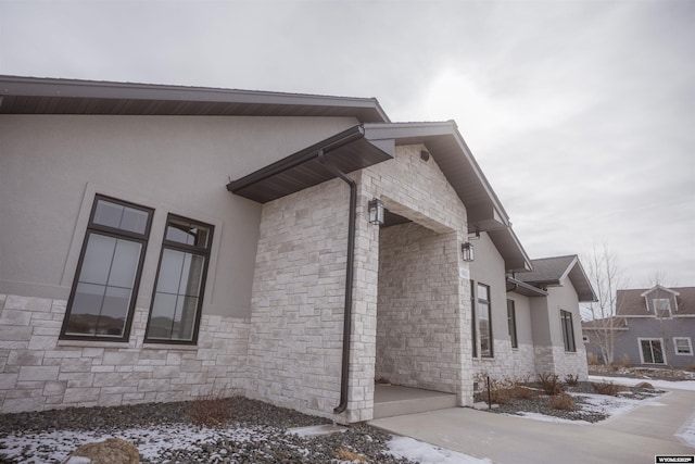 view of snow covered exterior with stone siding and stucco siding