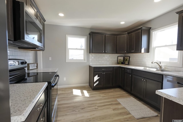 kitchen featuring stainless steel appliances, tasteful backsplash, a sink, light wood-type flooring, and baseboards