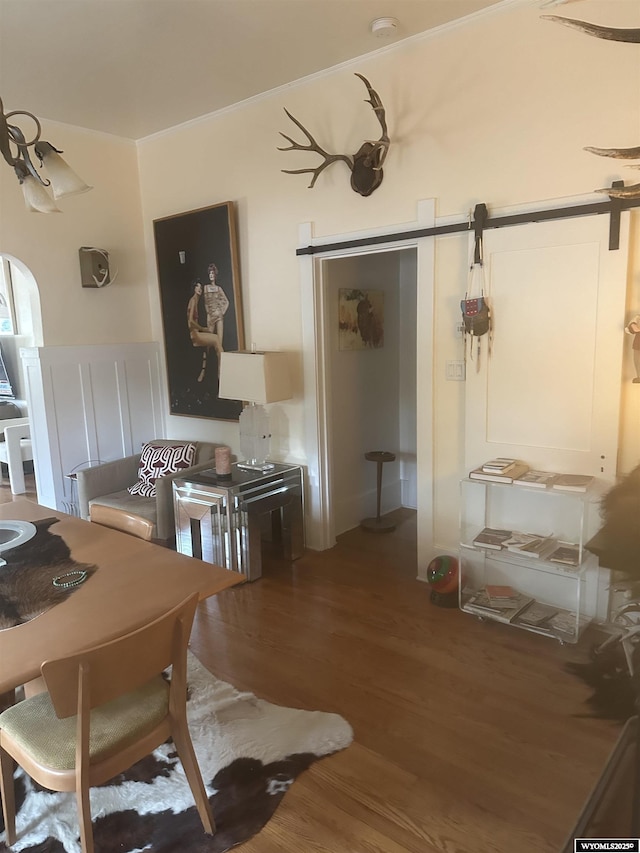 dining area with ornamental molding, a barn door, and wood finished floors