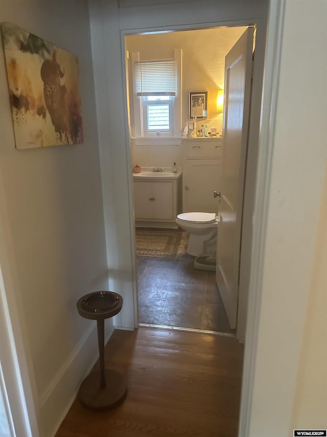 half bathroom with toilet, a sink, baseboards, and wood finished floors