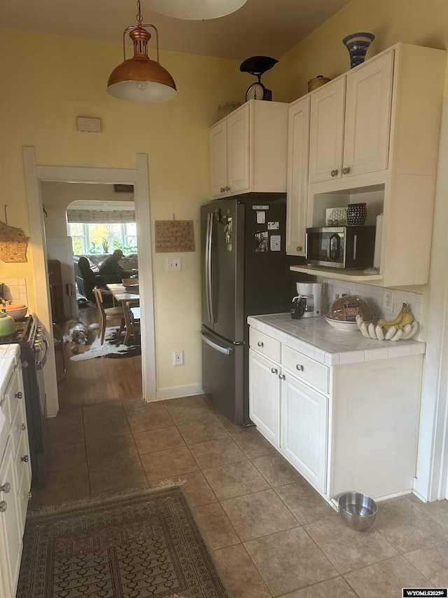 kitchen featuring tile countertops, hanging light fixtures, appliances with stainless steel finishes, white cabinetry, and light tile patterned flooring