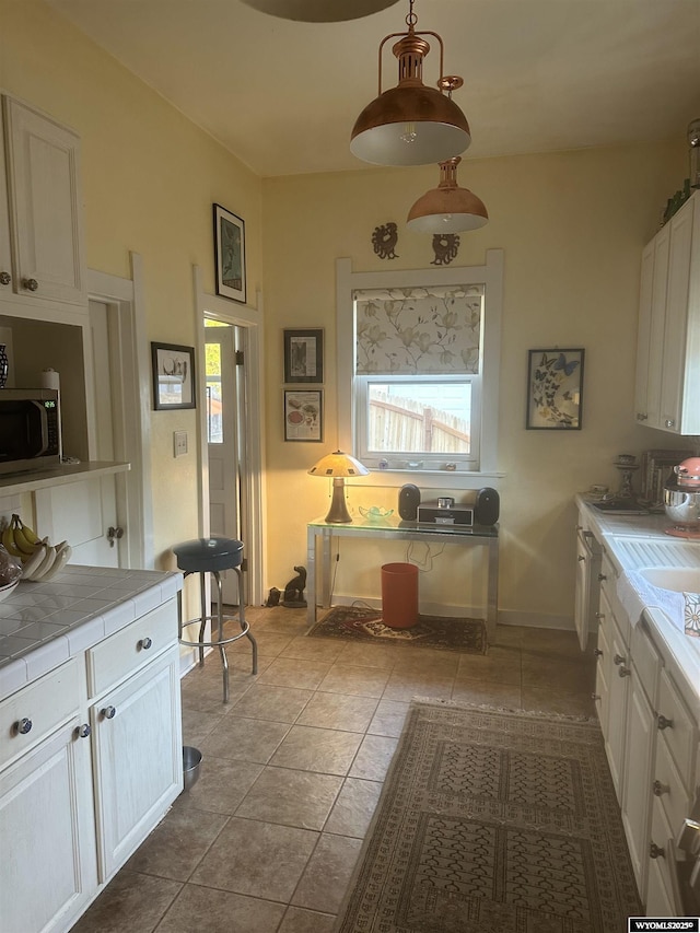 kitchen with stainless steel microwave, light tile patterned flooring, tile counters, and white cabinets