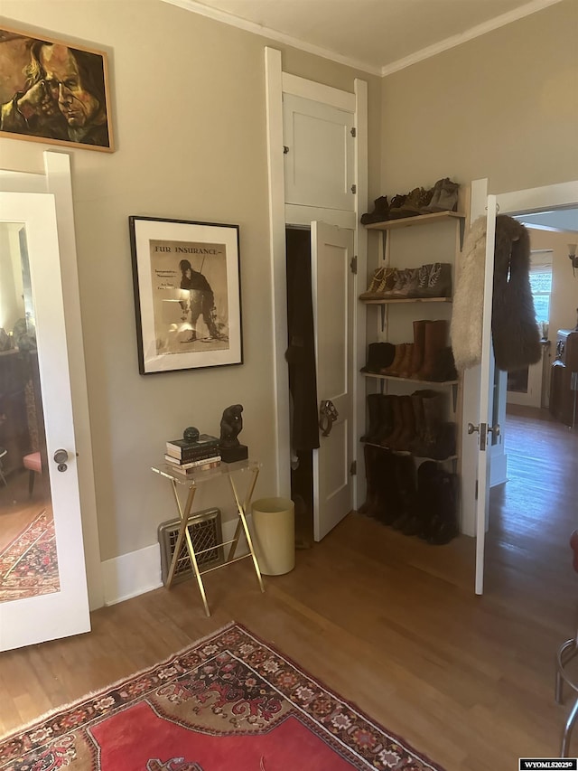 hall with baseboards, wood finished floors, visible vents, and crown molding