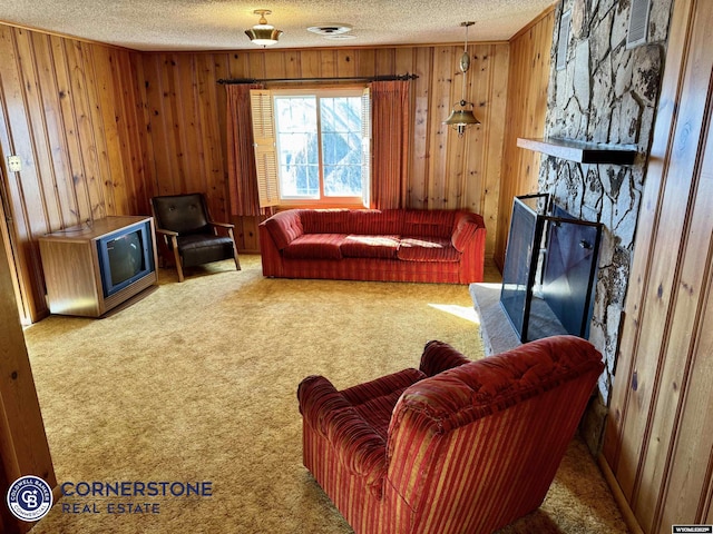 carpeted living room with wood walls, a textured ceiling, and a stone fireplace