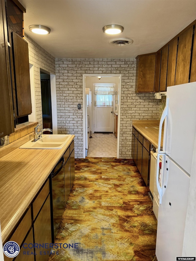 kitchen featuring black dishwasher, brick wall, freestanding refrigerator, light countertops, and a sink