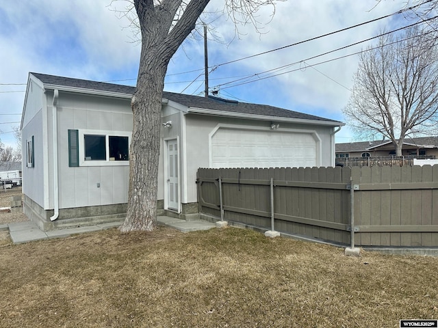 rear view of house with a garage, roof with shingles, fence, and a yard