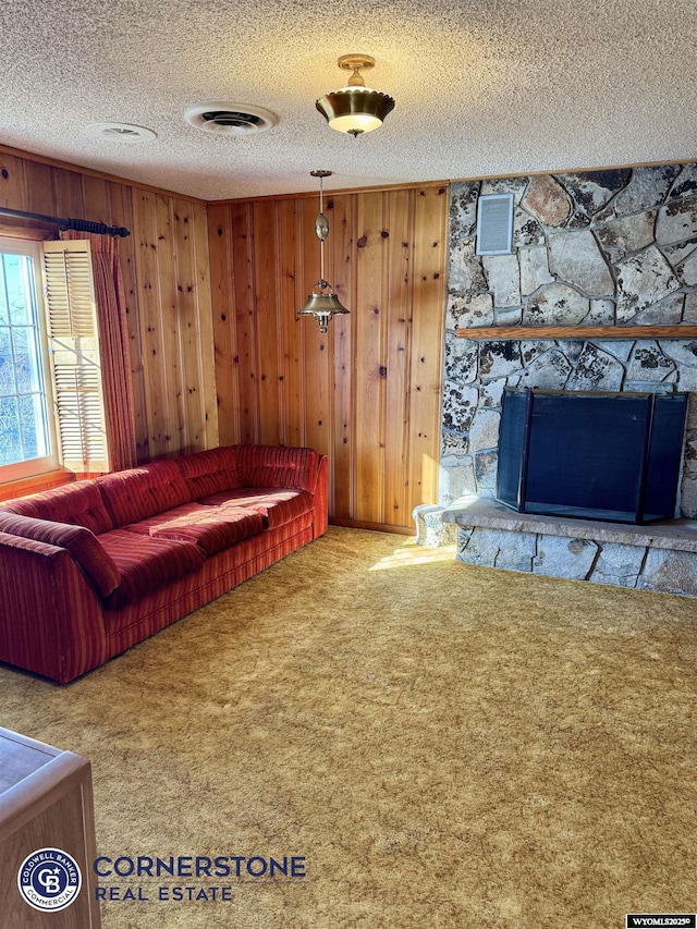 unfurnished living room featuring wooden walls, visible vents, a textured ceiling, carpet flooring, and a fireplace