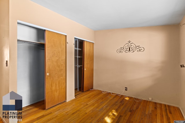 unfurnished bedroom with wood finished floors and two closets