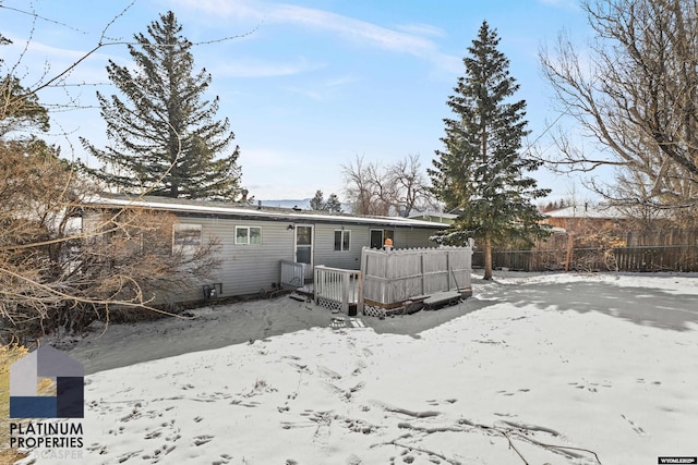 snow covered back of property with a deck and fence