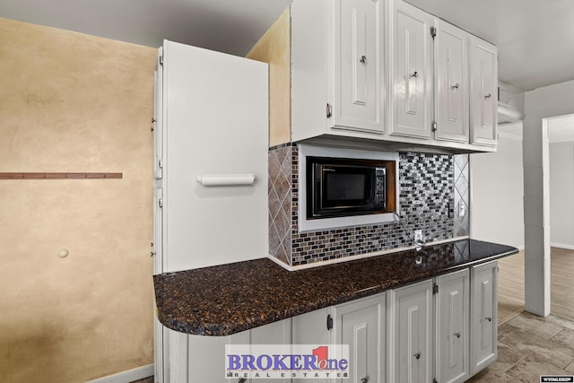 kitchen featuring black microwave, white cabinetry, baseboards, decorative backsplash, and dark stone counters