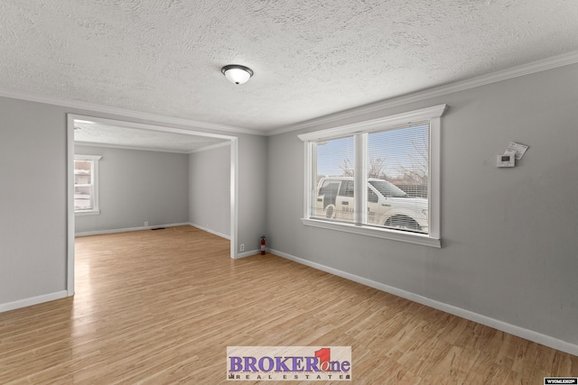 empty room with light wood-style flooring, a textured ceiling, ornamental molding, and baseboards