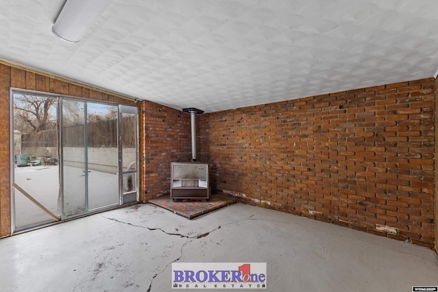 unfurnished living room with concrete flooring, lofted ceiling, a wood stove, and brick wall