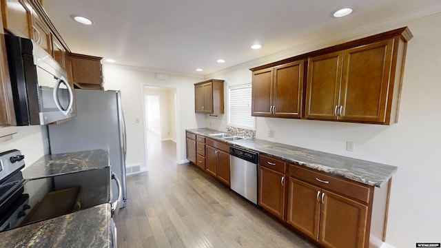 kitchen featuring brown cabinetry, light wood-style flooring, appliances with stainless steel finishes, dark stone countertops, and a sink