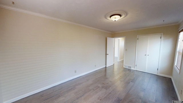 unfurnished bedroom with a closet, visible vents, ornamental molding, wood finished floors, and baseboards