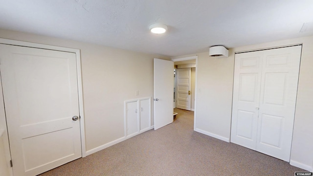 unfurnished bedroom featuring a closet, light carpet, and baseboards