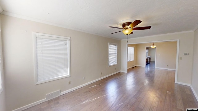 unfurnished room featuring ceiling fan, wood finished floors, visible vents, baseboards, and ornamental molding