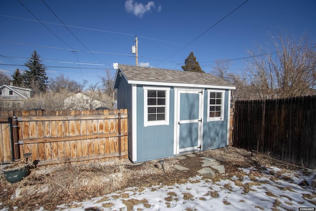 snow covered structure featuring an outbuilding, a fenced backyard, and a storage unit