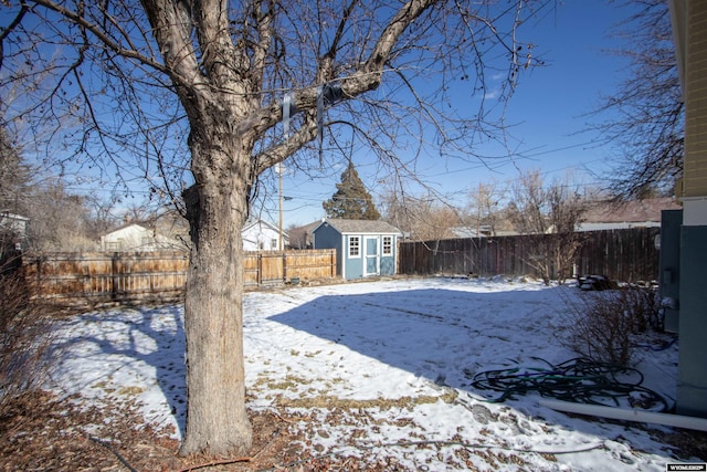 snowy yard featuring a fenced backyard, a storage unit, and an outdoor structure