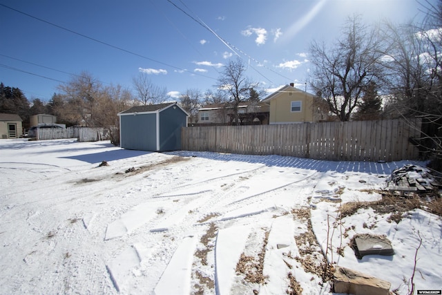 yard layered in snow featuring an outbuilding, fence, and a storage unit