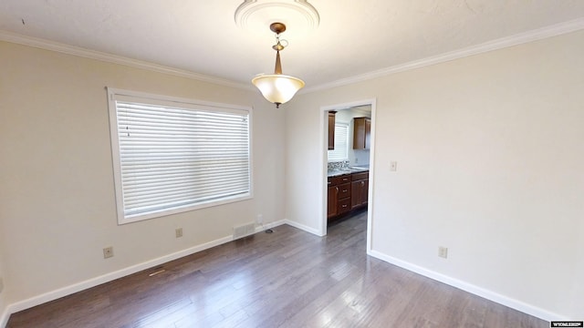 spare room with a sink, wood finished floors, visible vents, baseboards, and crown molding