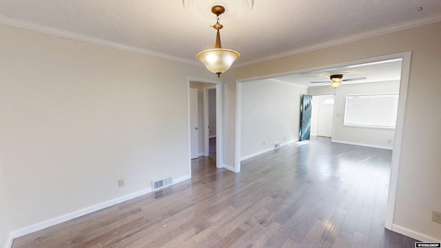 spare room featuring ceiling fan, wood finished floors, visible vents, baseboards, and crown molding