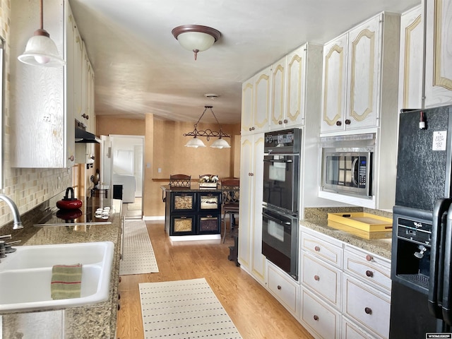 kitchen with light wood-style floors, under cabinet range hood, black appliances, pendant lighting, and a sink