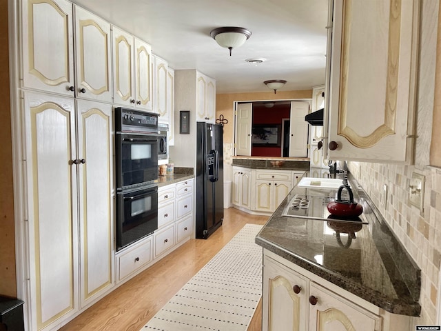 kitchen featuring light wood finished floors, tasteful backsplash, dark stone countertops, under cabinet range hood, and black appliances