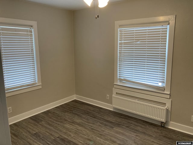 empty room featuring dark wood-type flooring, radiator, and baseboards