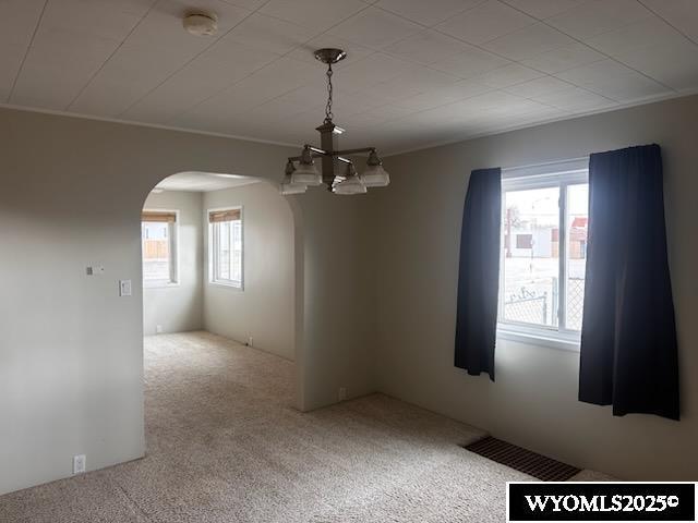 empty room with carpet floors, arched walkways, and visible vents