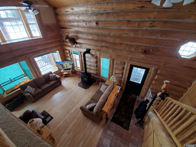 living area with a ceiling fan, lofted ceiling, a wood stove, and wood finished floors