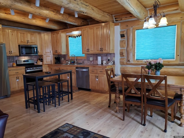 kitchen with appliances with stainless steel finishes, light wood-type flooring, a sink, and decorative light fixtures