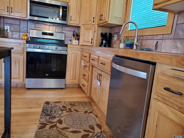 kitchen featuring light wood finished floors, light countertops, appliances with stainless steel finishes, and backsplash